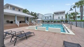 Une piscine avec des chaises longues, un espace de détente couvert et un bâtiment à la façade blanche.
