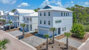 Une rangée de maisons modernes, blanches, à deux étages, avec des toits plats, une allée pavée et un ciel d’un bleu limpide.