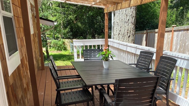 Una terraza de madera con una mesa, sillas, un felpudo y una pérgola.