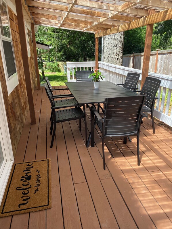 A wooden deck with a table and chairs, a welcome mat, and a pergola structure. - Cozy 3BR Bainbridge Island Home with Large Fenced Yard Near Ferry & Town (Bainbridge Island)
