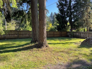 A fenced yard with a large tree, grass, and a wooden fence.