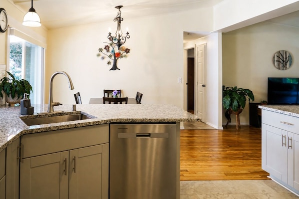 A kitchen with a granite countertop, stainless steel appliances, and a dining area with a table and chairs.