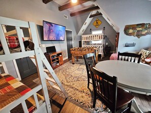 A cozy loft-style room with a television, wooden furniture, and a unique wall decoration. - Bunk/Game Room, Near Lake, Pet Friendly, Firepit, FUN! (Toccoa)