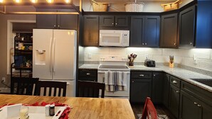 A kitchen with dark cabinets, a white refrigerator, a microwave, and a wooden dining table. - Bunk/Game Room, Near Lake, Pet Friendly, Firepit, FUN! (Toccoa)