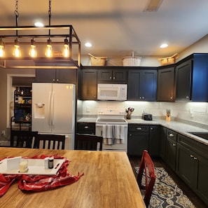A kitchen with dark cabinets, a white refrigerator, a microwave, and a wooden dining table. - Bunk/Game Room, Near Lake, Pet Friendly, Firepit, FUN! (Toccoa)