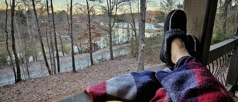 Henkilö rentoutuu kuistilla, josta avautuu näkymä puihin ja vesistöön.