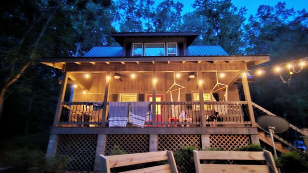 A wooden deck with string lights, a covered seating area, and a view of the surrounding forest. - Bunk/Game Room, Near Lake, Pet Friendly, Firepit, FUN! (Toccoa)