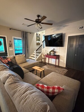 Un salon comprenant un canapé, une table basse, un téléviseur fixé au mur et un ventilateur de plafond.