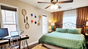 Ein Schlafzimmer mit Bett, Schreibtisch, Computer und einer an der Wand befestigten Tennisausrüstung.