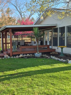 A covered patio with outdoor furniture, a small house-shaped decoration, and a palm tree. - The Lil Lazy Lakehouse
 Hillsdale Mi,                           
3BR, 1 bath (Hillsdale)