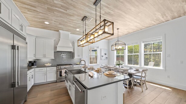 Une cuisine moderne avec des meubles blancs, un îlot central, des appareils en acier inoxydable et un plafond en bois.