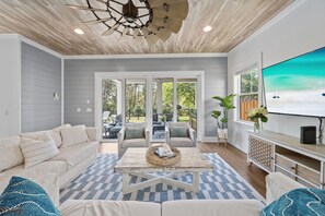 A living room with a sofa, coffee table, and TV, a ceiling fan, and a view through glass doors to an outdoor area. - .5 miles to beach~Private Pool~Dogs OK~EV Charger (Santa Rosa Beach)