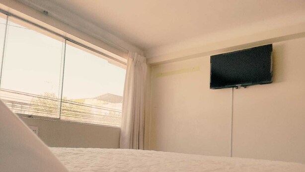 Una habitación de hotel con una cama, una ventana con cortinas y un televisor montado en la pared.