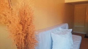 Una habitación con un sofá blanco, una planta seca alta y una puerta al fondo.