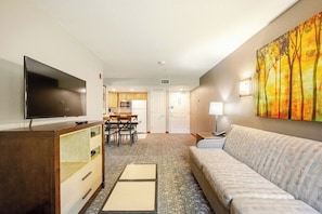 A hotel room with a flat-screen TV, a sofa, a dining area with a table and chairs, and a kitchen in the background. - WorldMark Canmore - Banff  - One Bedroom Unit (Canmore)
