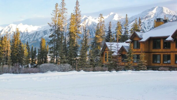 Un chalet en bois doté de plusieurs pièces, entouré de montagnes enneigées et de grands pins.