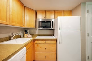 A compact kitchen with wooden cabinets, a stainless steel microwave, a white refrigerator, and a dishwasher. - WorldMark Canmore - Banff  - One Bedroom Unit (Canmore)