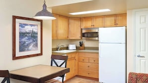 Une cuisine compacte avec des meubles en bois, un réfrigérateur blanc, un four à micro-ondes, un évier et un coin repas comprenant une table et des chaises.