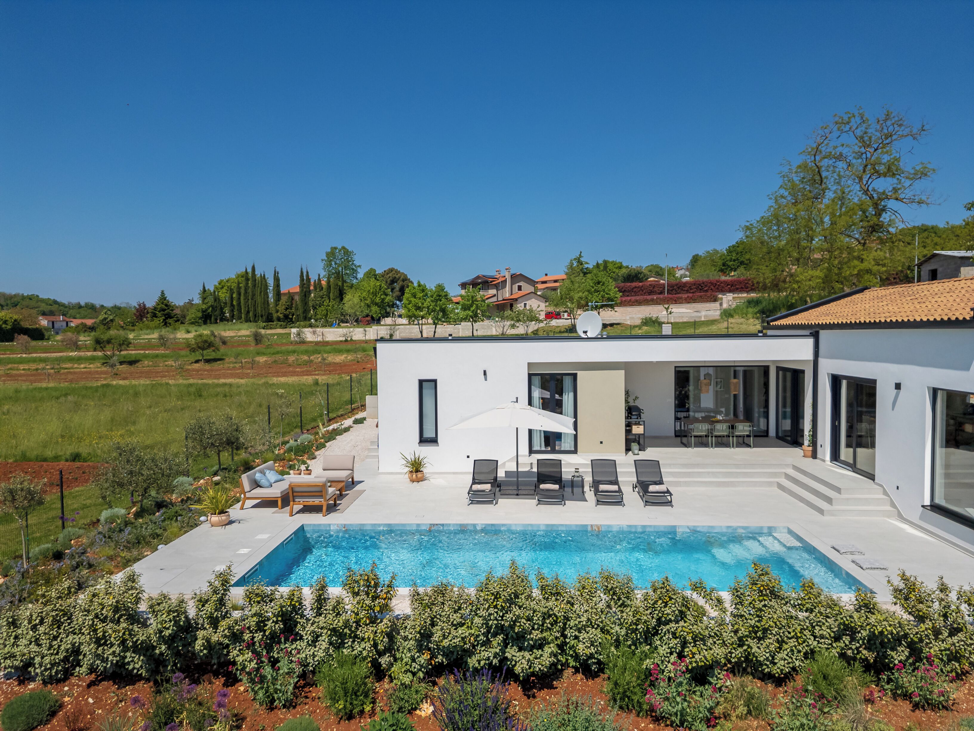 A modern house with a swimming pool, outdoor seating, and a view of the countryside.