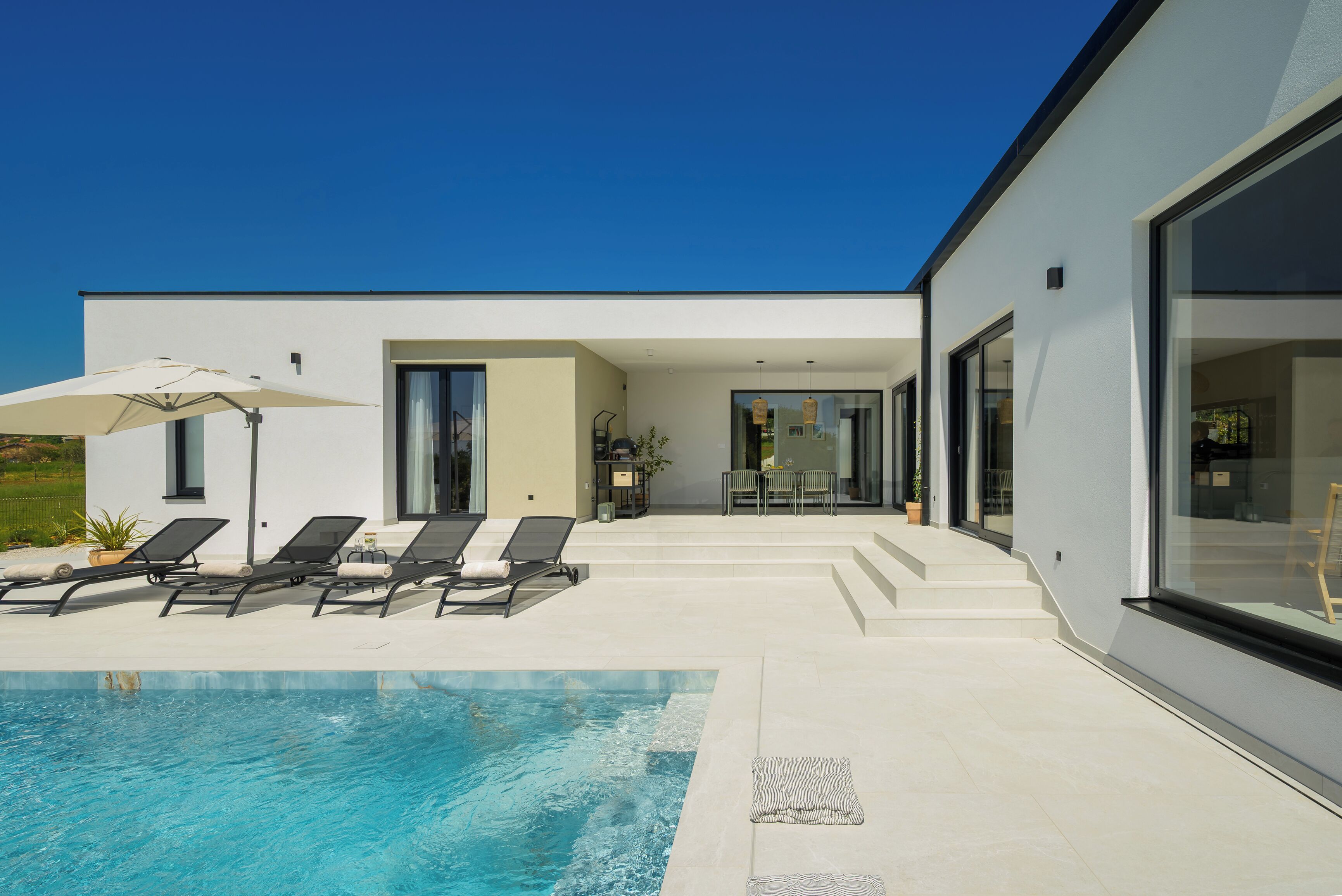 A modern house with a swimming pool, sun loungers, and a patio area.