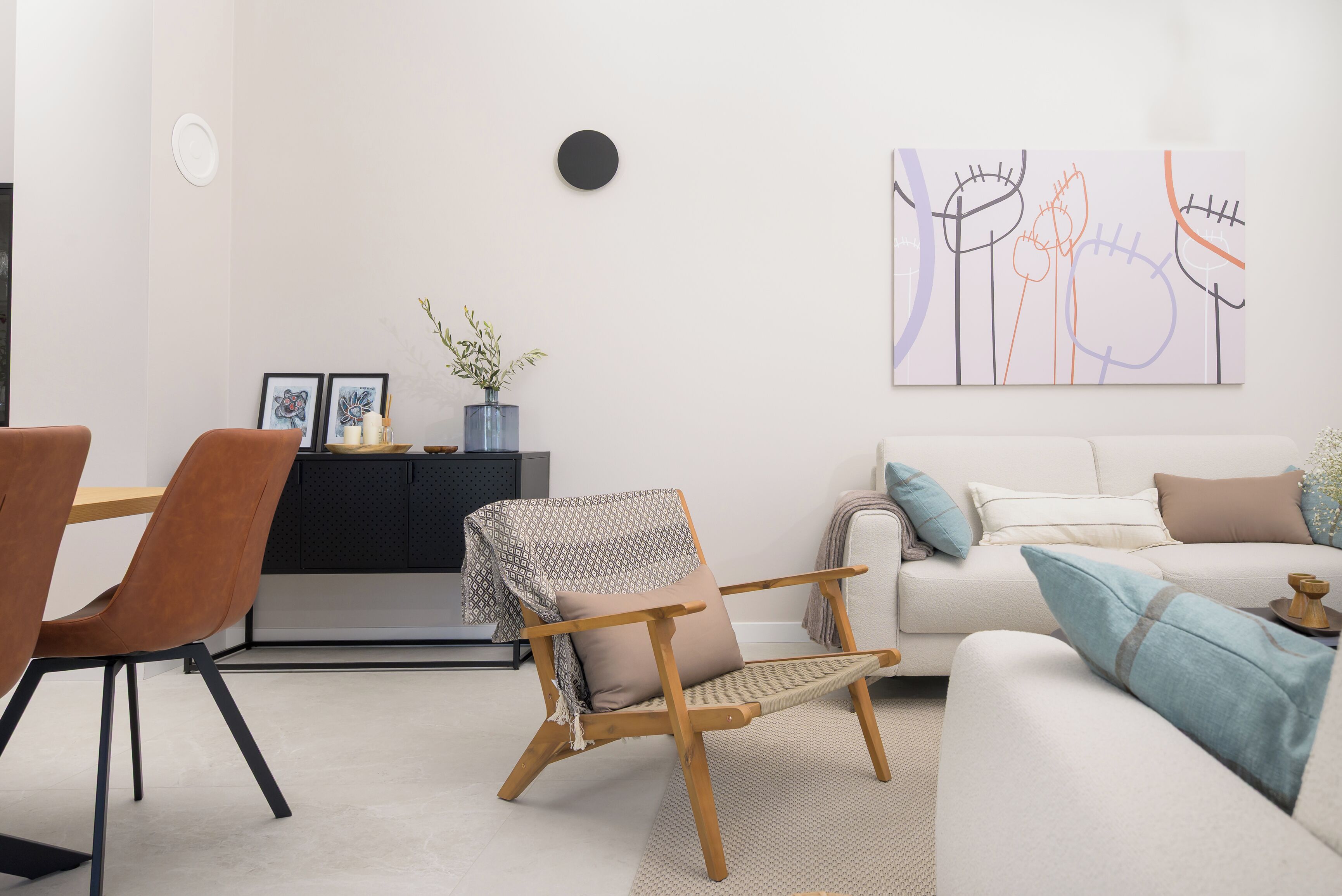Un salon moderne comprenant un canapé, une chaise en bois, une table à manger avec des chaises et une œuvre d’art accrochée au mur.