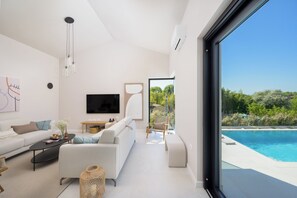 A modern living room with a large window, a flat-screen TV, a sofa, a coffee table, and a pool view. - Villa Modrić (Istria - Pazin) (Pazin)