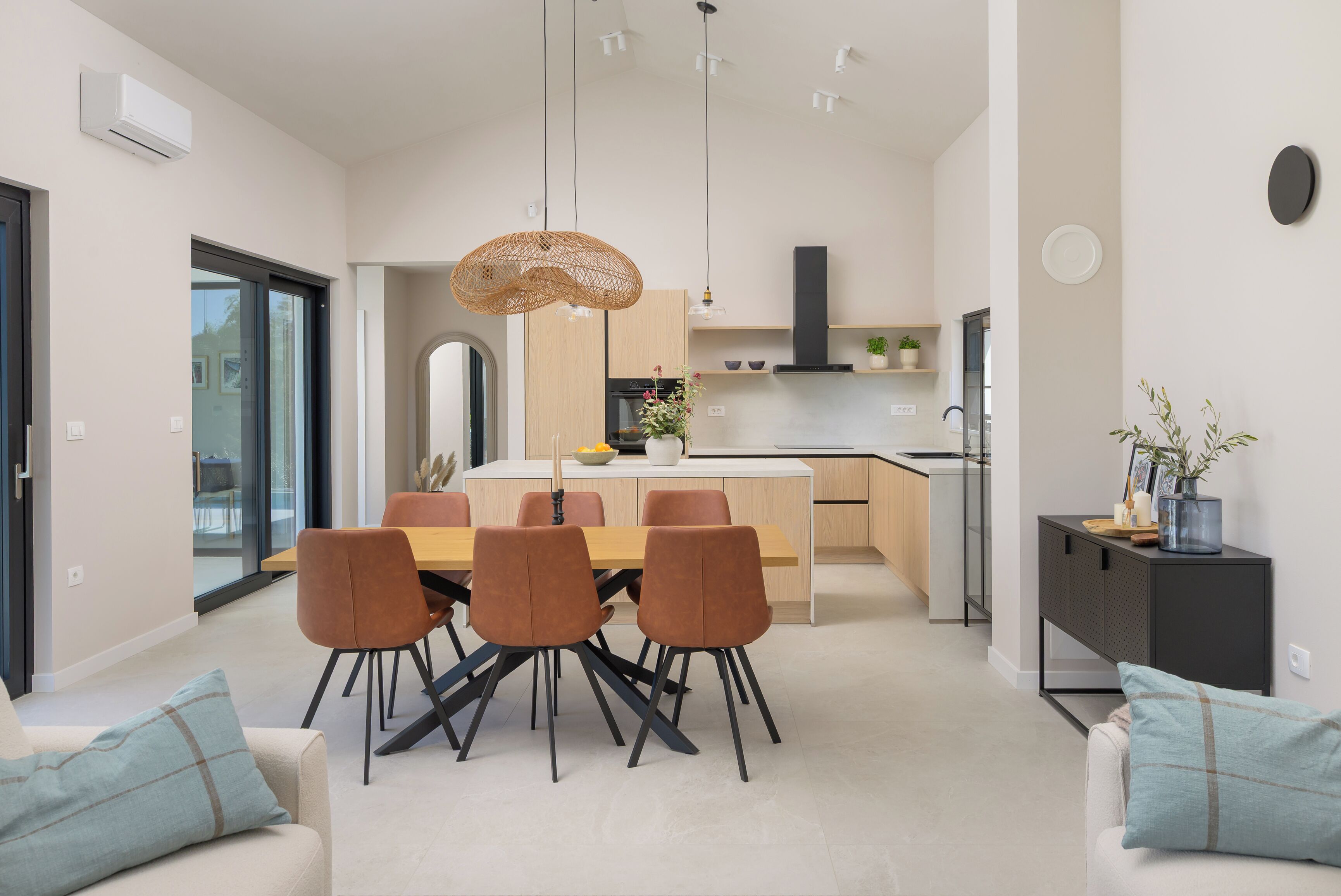 A modern kitchen with a dining area, featuring a central island, pendant lighting, and a view of the adjacent dining room.