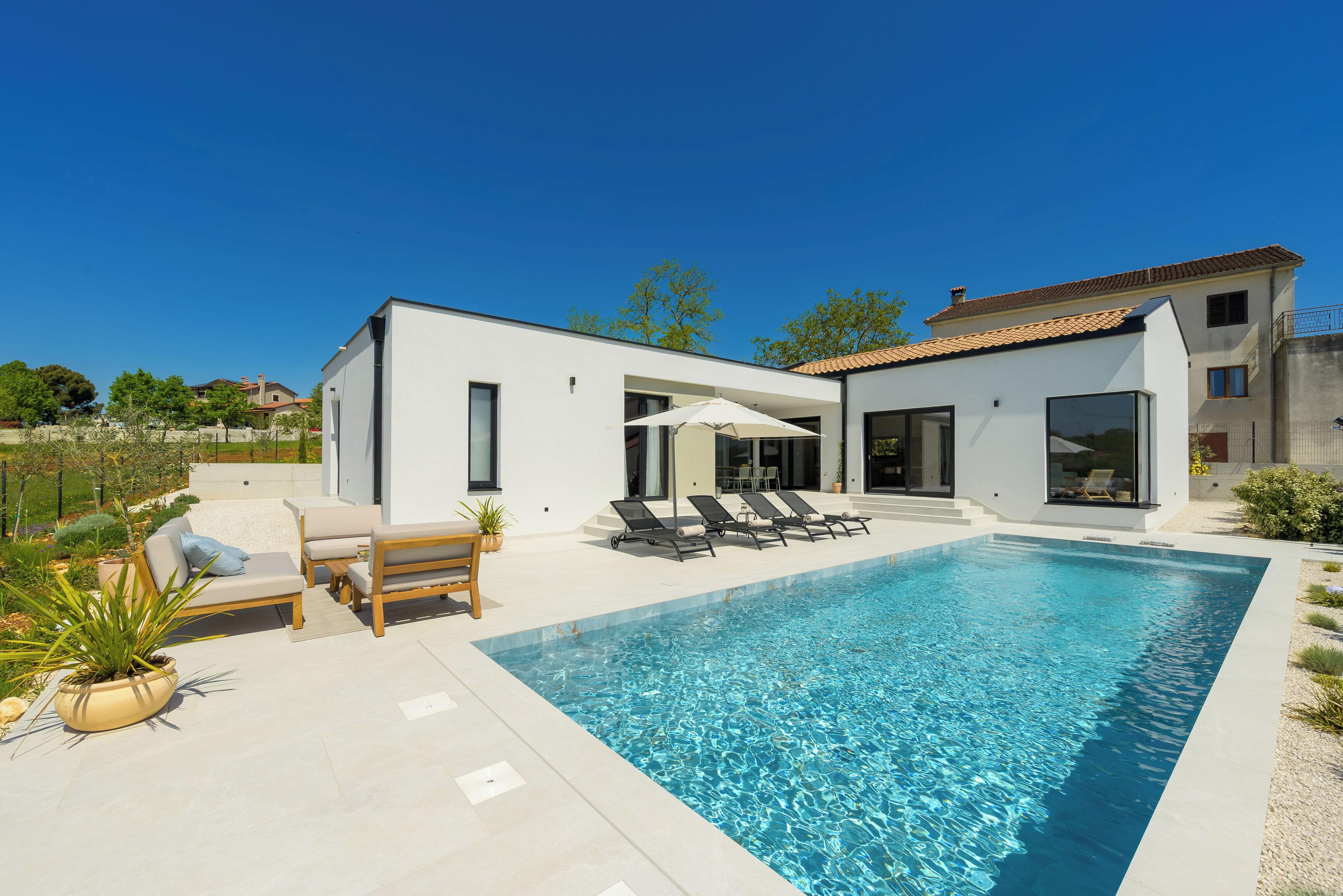 Une maison moderne dotée d’une piscine, d’un espace salon extérieur et d’un jardin.
