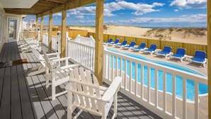A wooden deck with white railings, a pool with blue chairs, and a view of the beach. - Dmanfish - Oceanfront 9 BR w/pool (Virginia Beach)