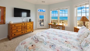 A bedroom with a bed, a dresser, a television, a desk, and a view of the beach. - Dmanfish - Oceanfront 9 BR w/pool (Virginia Beach)