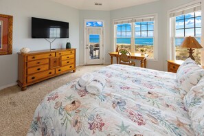 Ein Schlafzimmer mit Bett, Kommode, Fernseher, Schreibtisch und Blick auf den Strand.