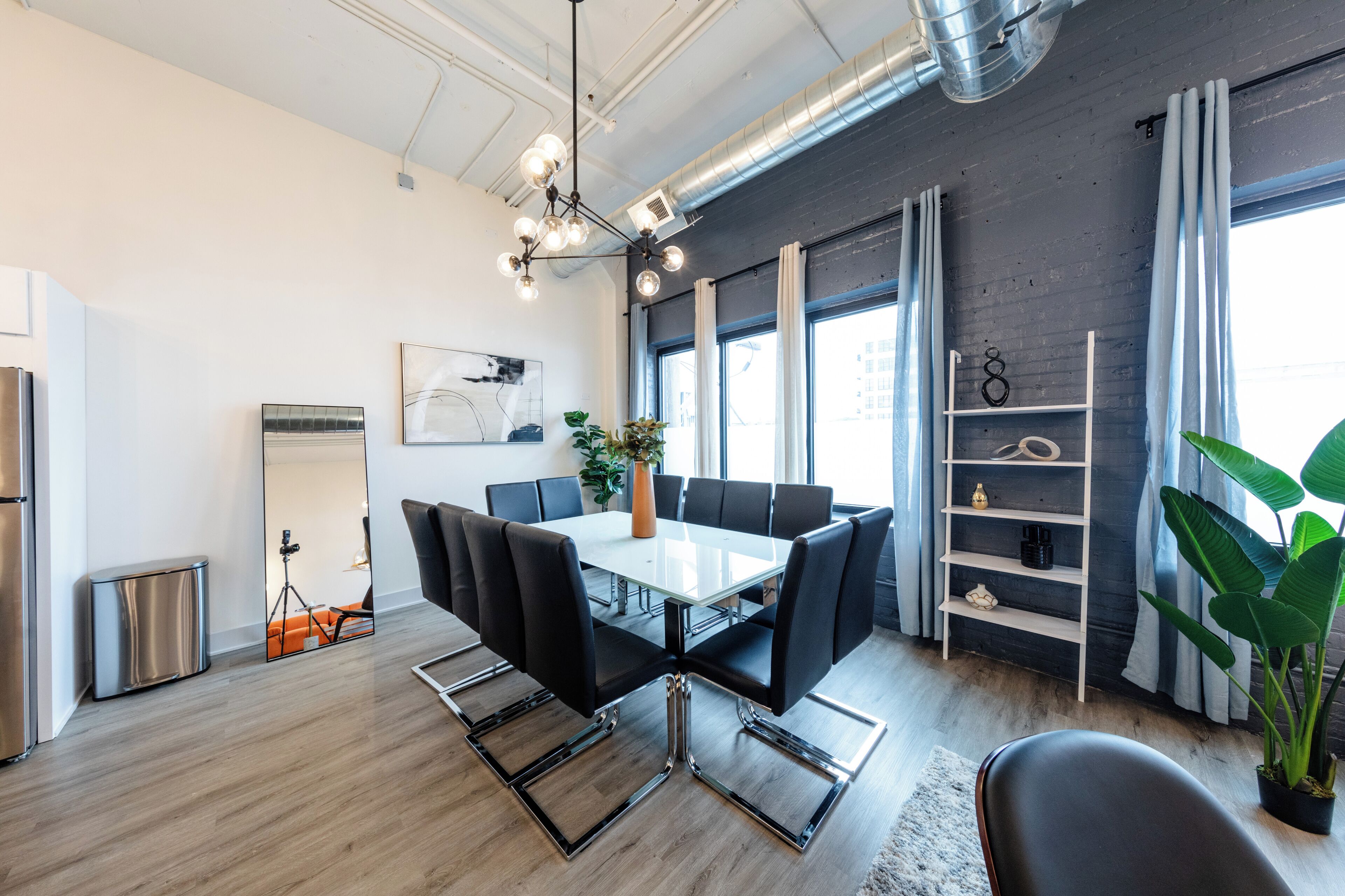 A modern dining area with a glass-top table, black chairs, and a chandelier.