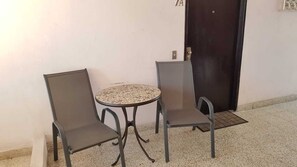 Ein kleiner runder Tisch mit zwei Stühlen, eine dunkle Tür und eine weiße Wand.