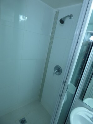 Eine Duschkabine mit Glas, eine geflieste Wand, eine Duschbrause und ein Waschbecken mit Spiegel.
