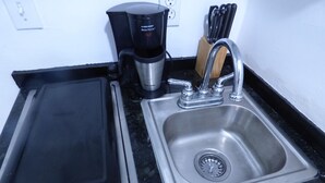 Et køkken med en stålvask, kaffemaskine og et knivdisplay.