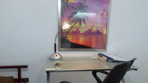 En arbejdsplads med et skrivebord, stol og et indrammet billede af en solnedgang.