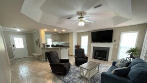 A spacious living area with a ceiling fan, a fireplace, a large TV, and a kitchen in the background. - Beautiful 3-bedroom home near Southeast hospital and downtown Dothan (Dothan)