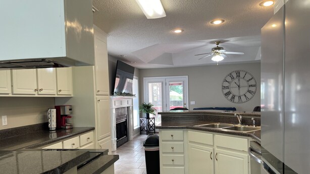 A kitchen with white cabinetry, a granite countertop, a stainless steel refrigerator, a ceiling fan, and a wall clock. - Beautiful 3-bedroom home near Southeast hospital and downtown Dothan (Dothan)