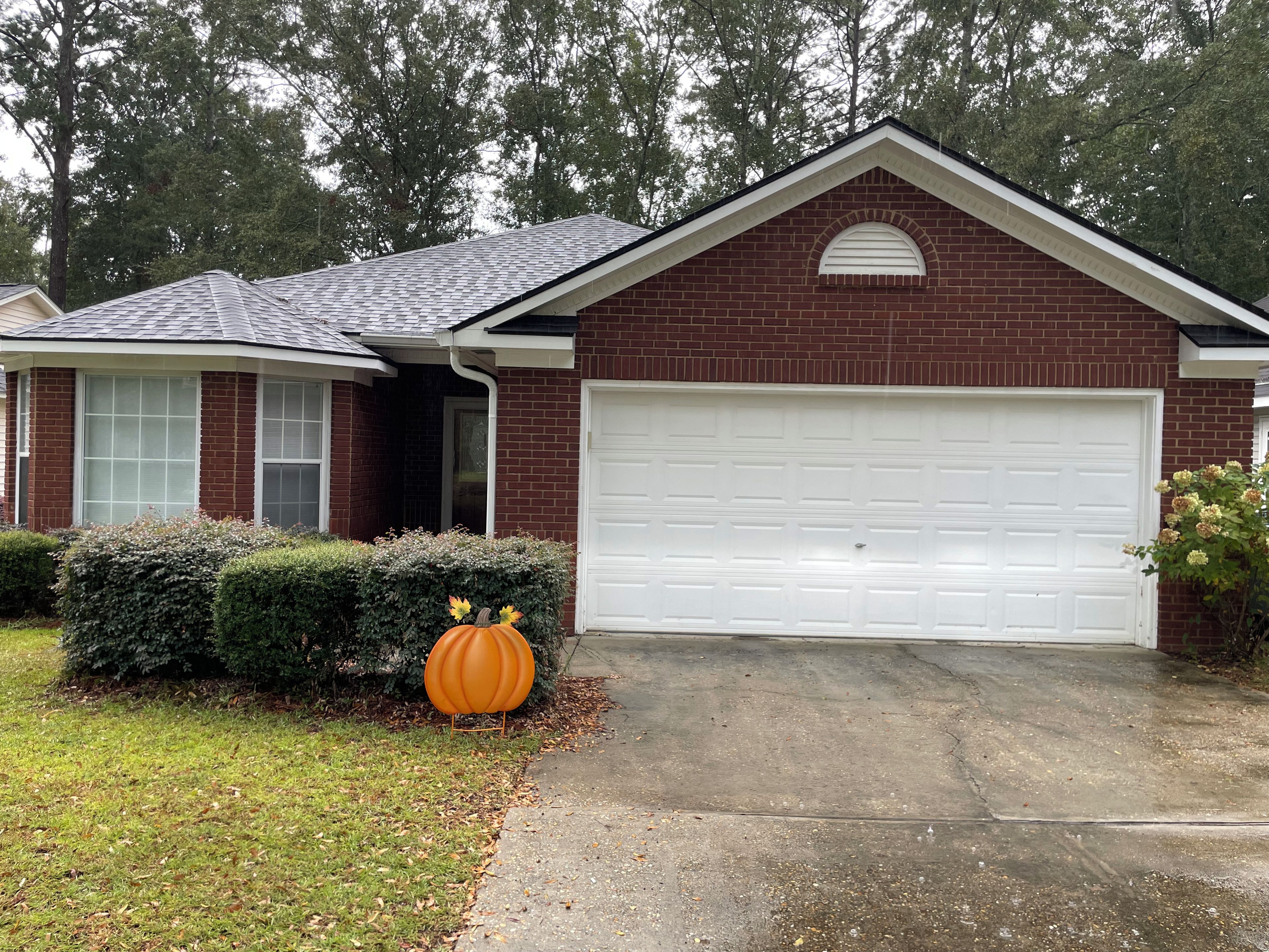 A residential house with a garage, brick exterior, and a lawn with a decorative pumpkin.