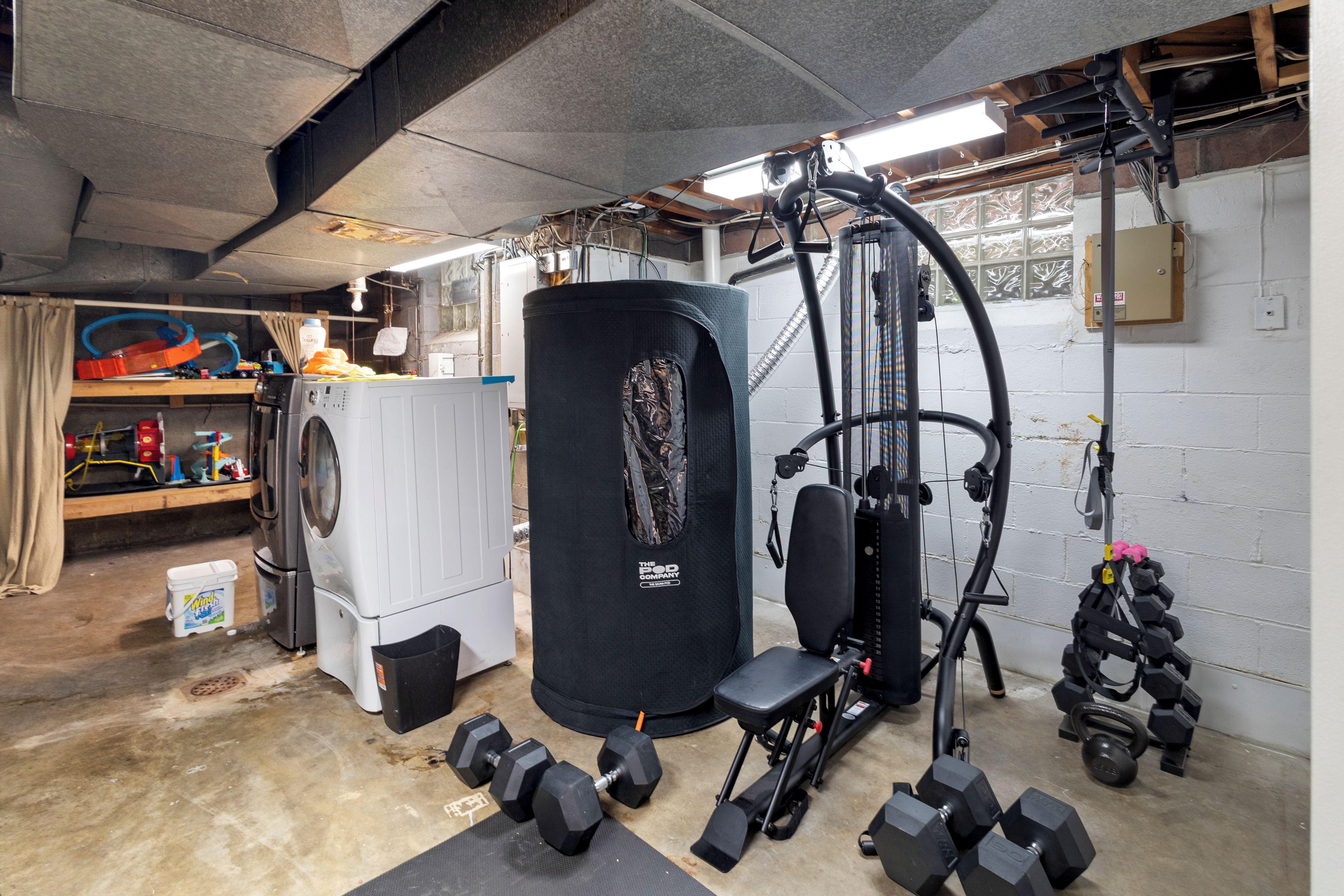 Un gimnasio en casa con equipo de ejercicio, una lavadora y un tanque de agua grande.