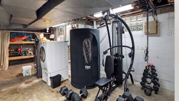 Un gimnasio en casa con equipo de ejercicio, una lavadora y un tanque de agua grande.