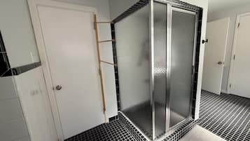 Un baño con cabina de ducha, suelo de baldosas y una puerta blanca.