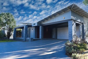 A modern two-story house with a garage, stone pillars, and a covered driveway. - Jasmine Escape |Architect-Designed Bush Retreat, Pool, Sunken Spa & Fire Pit (Ellalong)