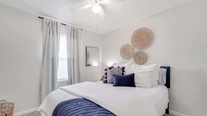 Une chambre à coucher avec un lit, un ventilateur de plafond, une fenêtre avec des rideaux et des éléments de décoration murale.