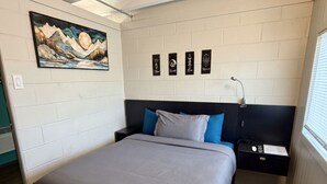 Un dormitorio con una cama, una mesita de noche, una lámpara de pared, un cuadro y cuatro elementos enmarcados en la pared.