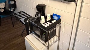 Une petite cuisine équipée d’un four à micro-ondes, d’une machine à café et d’un petit réfrigérateur. Un téléviseur à écran plat est fixé au mur, au-dessus du comptoir.