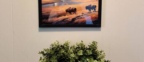 A framed Yellowstone National Park poster on a wall, a gray felt planter with green plants below it, and a black shelf.
