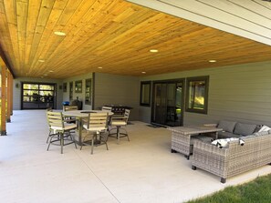 Eine Terrasse im Freien mit Holzboden, einem Tisch mit Stühlen, einer Korbschaukel und einem Grill.