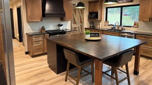 Een moderne keuken met houten kastjes, een centraal eiland, hanglampen en uitzicht op de omgeving.