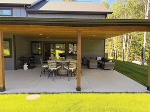 Un patio techado con una mesa y sillas, una parrilla y asientos exteriores.